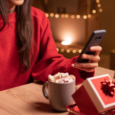 Woman holding phone and credit card next to holiday decorations